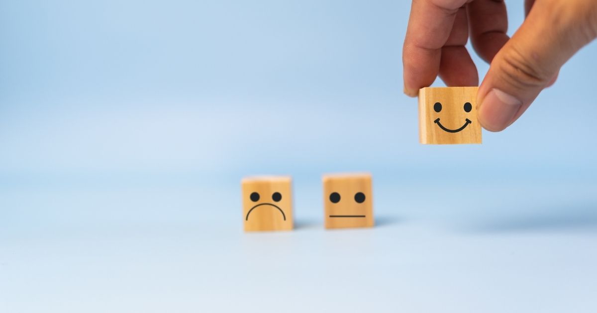 A hand holding a cube with a smile faces drawn on it.