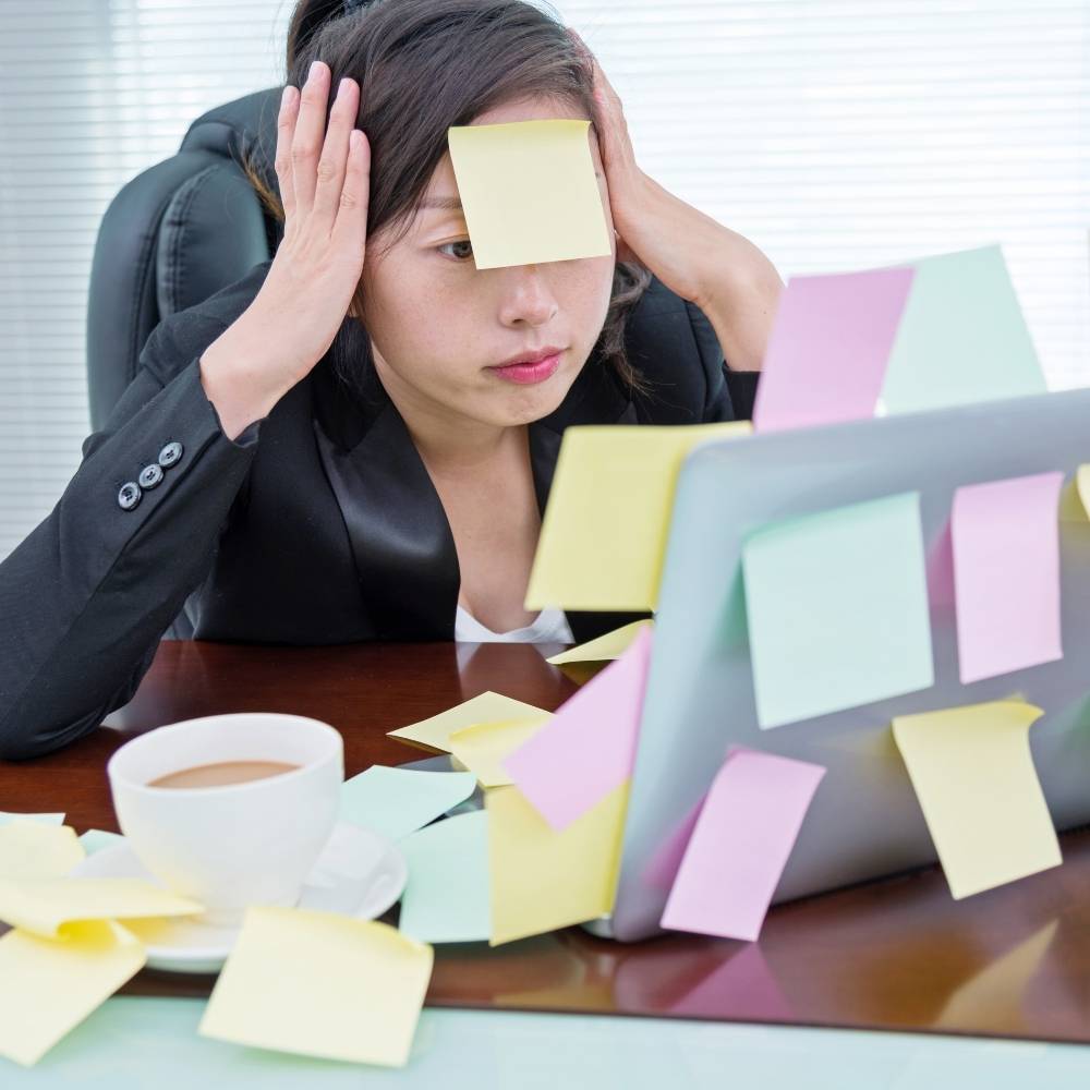 a Lady stressed in front of a PC with a post it on her head